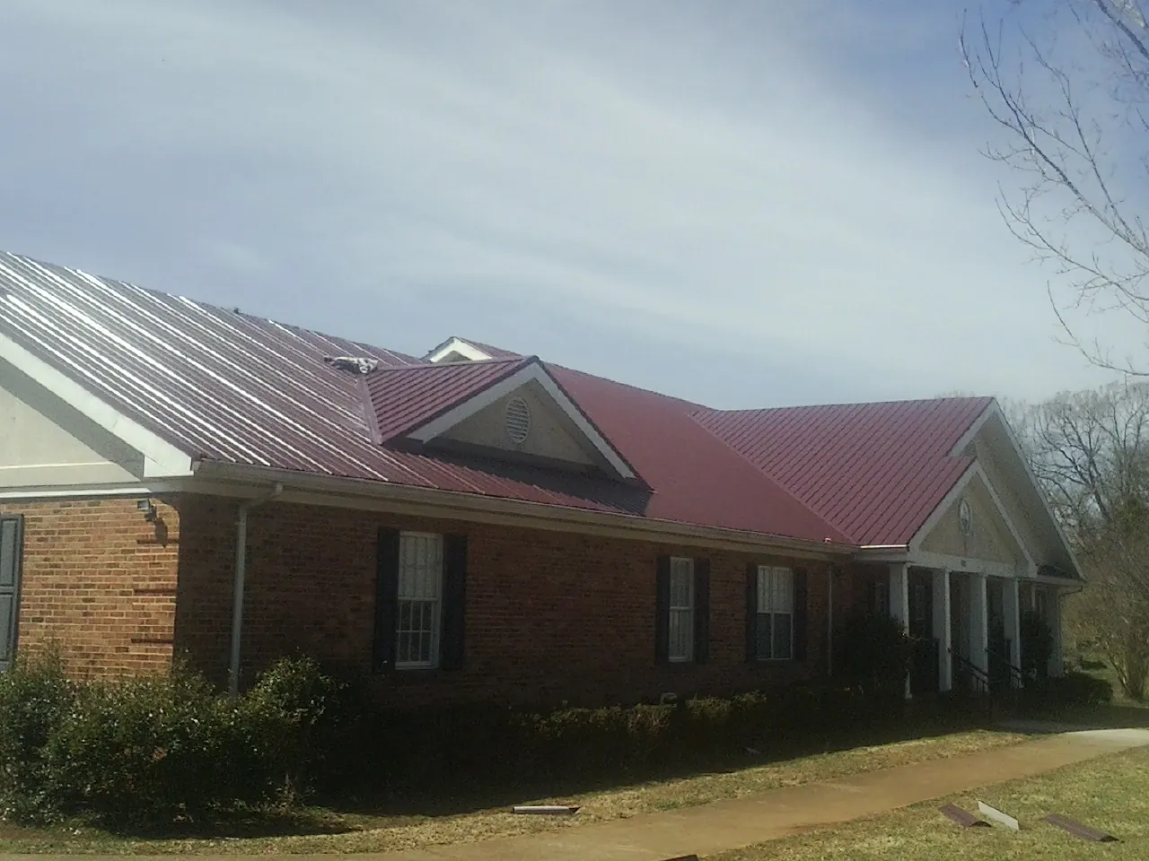 Red metal roof with gabled entries on a long brick building, from a Hail Damage Roof Repair job in Landisville
