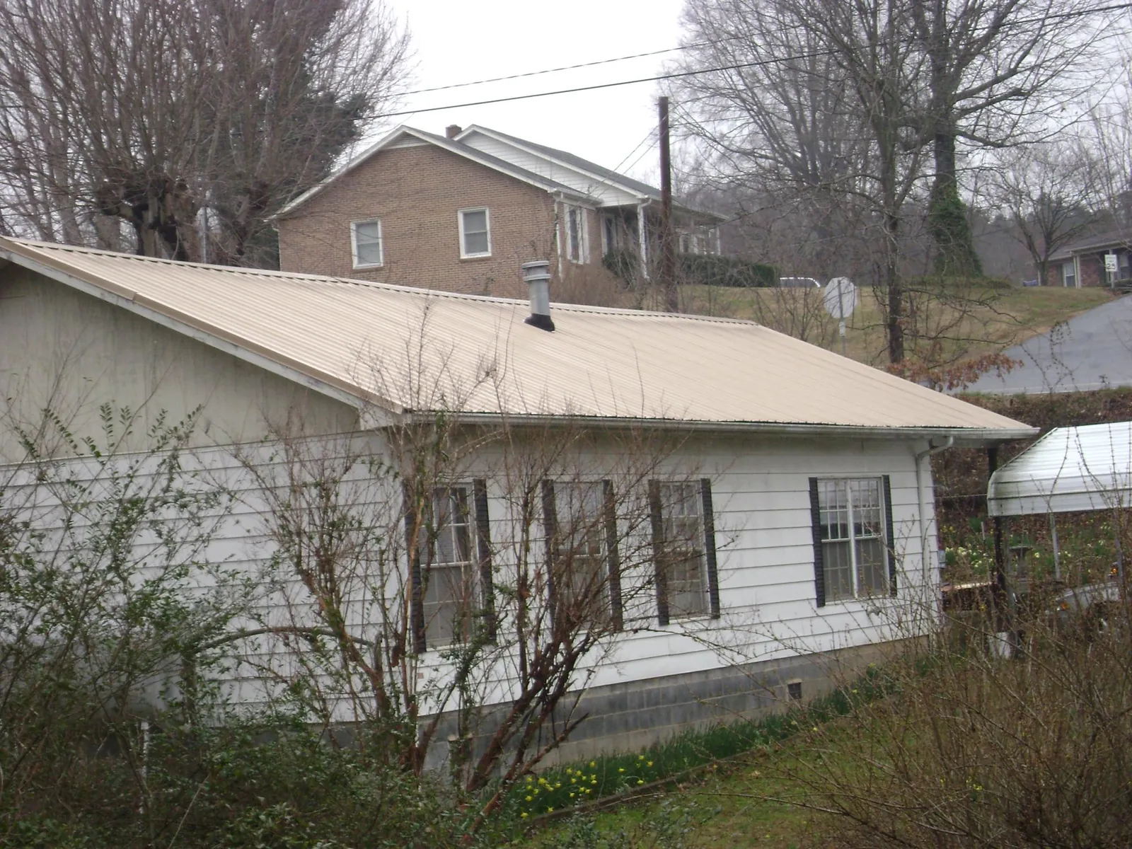 Tan metal roof on a white sided house set into a hillside — Commercial Roofing by Roofing Brothers in Landisville
